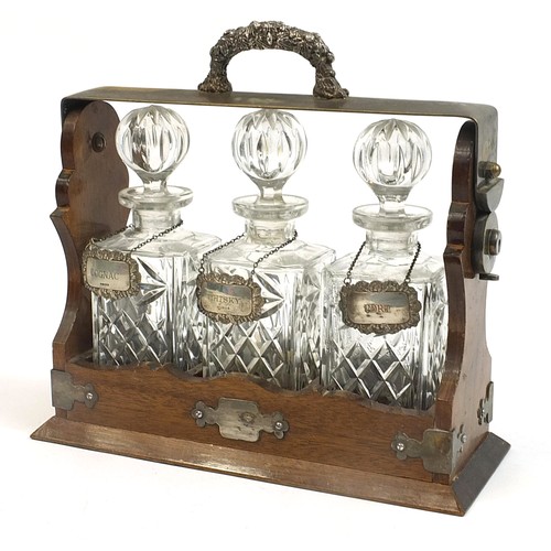 15 - Silver plated and oak three bottle tantalus with three glass decanters and three decanter labels, tw... 