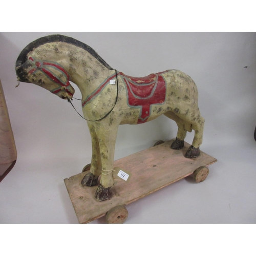 112 - Painted paper mache pull-along toy horse on a painted wooden base with four wheels, 25ins long overa... 