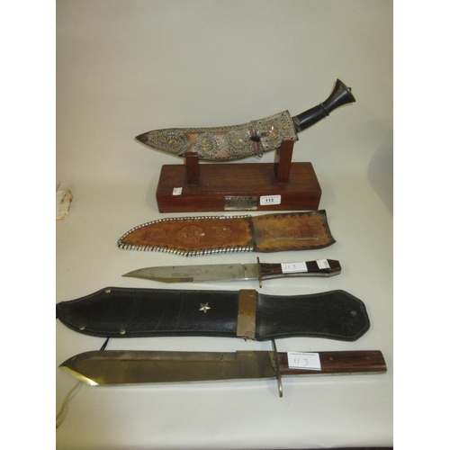 113 - Indian kukri with decorative scabbard on a display stand together with two reproduction Bowie knives