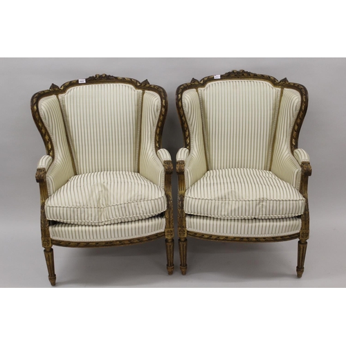 1570 - Pair of 19th Century French carved giltwood wing arm salon chairs upholstered in a striped cream fab... 