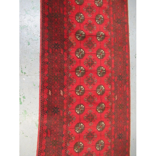 26 - Afghan runner with two rows of gols on a red ground with borders, 9ft 6ins x 2ft 10ins approximately