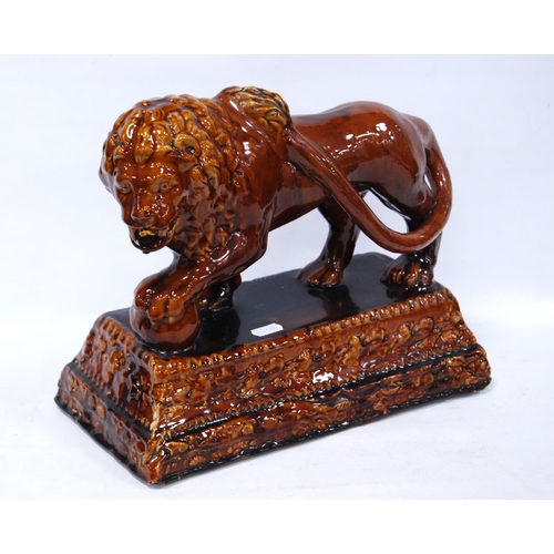 402 - 19th century treacle salt glazed stoneware model of a lion, the forepaw raised on a globe, on a step... 