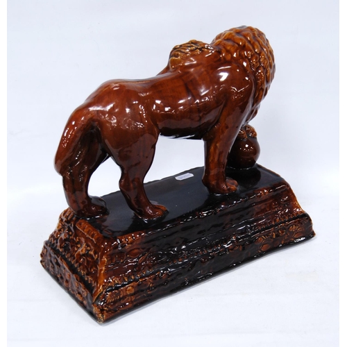 402 - 19th century treacle salt glazed stoneware model of a lion, the forepaw raised on a globe, on a step... 