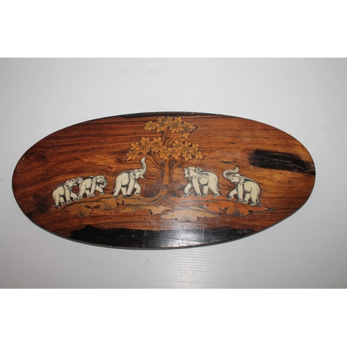 26 - Oval rosewood plaque with inlaid scene depicting elephants beneath a tree, 37cm.